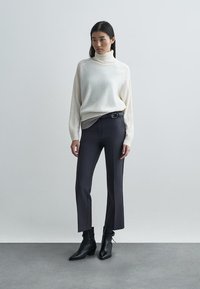 Μπεζ πουλόβερ με ζιβάγκο και ριμπ λεπτομέρειες, συνδυασμένο με σκουρόχρωμο παντελόνι με ψηλή μέση και μαύρα μποτάκια αστραγάλου με μύτη.