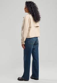 Beige, kevyt, lyhyt takki, jossa on takana läppäyksikkö, yhdistettynä tummansinisiin korkeavyötäröisiin farkkuihin. Mustat platform-kengät täydentävät asua.