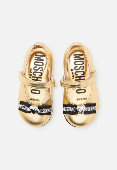Goldene metallische Babyschuhe mit einem Riemen, ausgestattet mit einem schwarzen Band, auf dem "Moschino" steht und einem silbernen Herzakzent an der Spitze. Hergestellt in Italien.