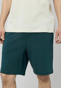 Shorts en coton teal avec poches latérales, taille élastique et coupe droite. Associés à un haut crème à manches courtes.