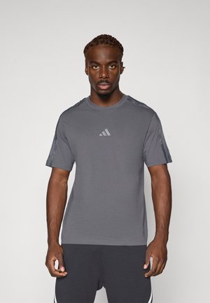 T-shirt gris à manches courtes avec un col rond, présentant un motif texturé sur les épaules et un logo discret sur la poitrine.
