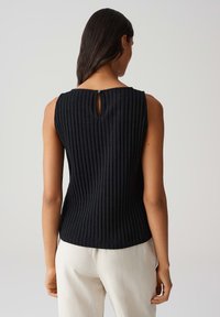 Top senza maniche nera con texture a coste verticali, apertura a chiave sul retro e design aderente che valorizza la silhouette.