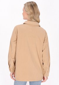 Tan kord skjorte med en afslappet pasform, der har krave, lange ærmer og lodret ribbet tekstur. Diskret bag søm detalje.