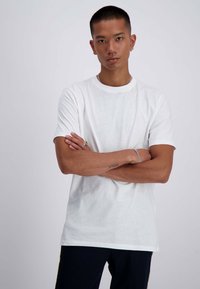 T-shirt bianco in cotone con collo rotondo e maniche corte. Il tessuto sembra morbido e ha una consistenza liscia, con una vestibilità comoda.