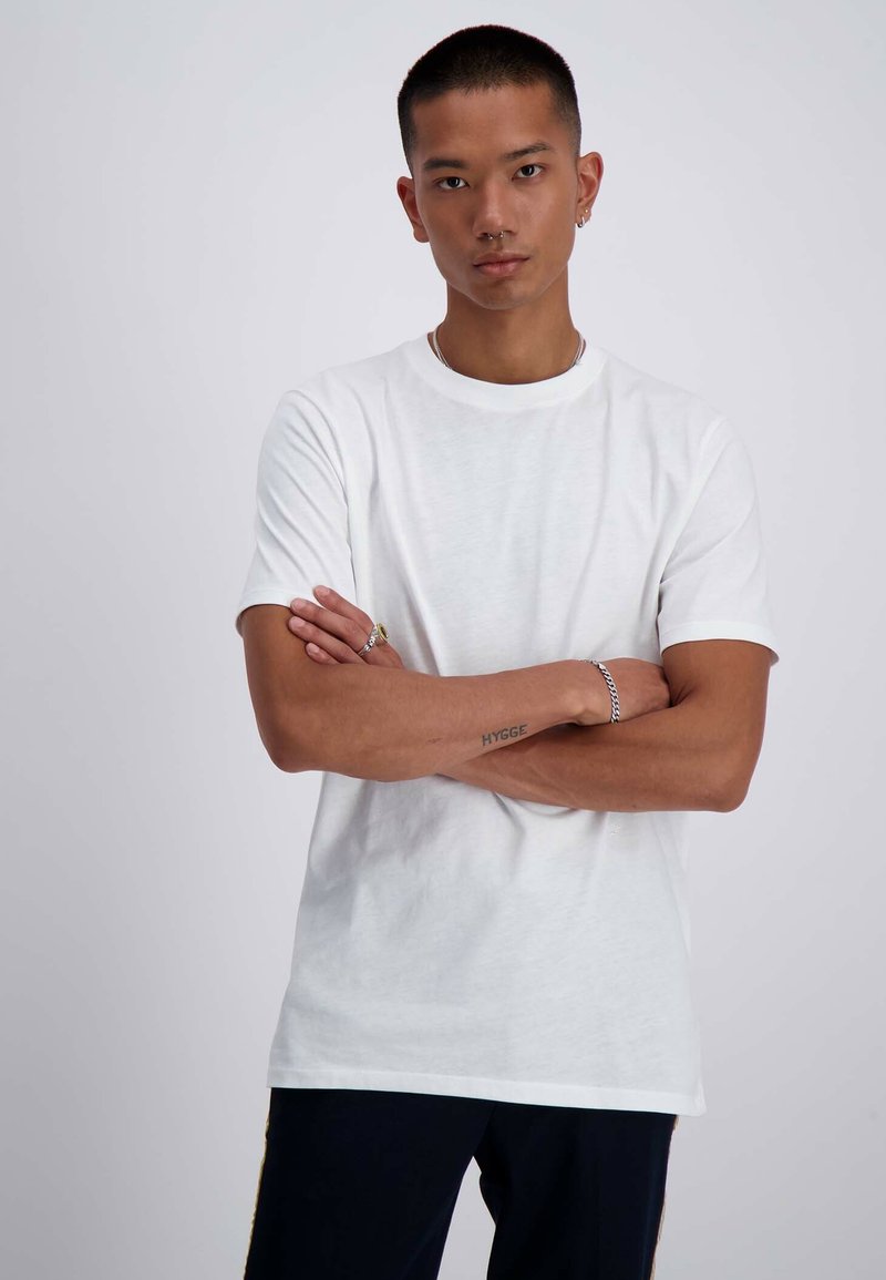 T-shirt bianco in cotone con collo rotondo e maniche corte. Il tessuto sembra morbido e ha una consistenza liscia, con una vestibilità comoda.