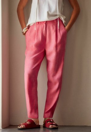 Rosa Leinenhose mit lässigem Schnitt, ausgestattet mit Seitentaschen und einem elastischen Bund; kombiniert mit roten Riemchensandalen mit Schnallen.