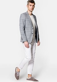 Szary pikowany marynarka na białej bluzce z dekoltem w serek, w połączeniu z białymi spodniami i szarymi trampkami. Marynarka ma fakturowany materiał i dwa guziki.