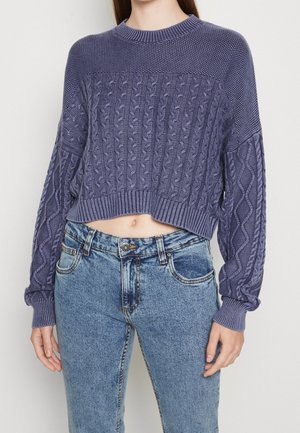 Gebreide paarse cropped trui met kabelbreipatroon, gebreide halslijn en manchetten, gecombineerd met lichtblauwe high-waisted denim jeans.