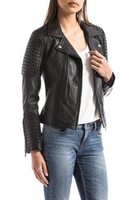 Schwarze Leder-Motorradjacke mit gesteppten Schulterdetails, asymmetrischem Frontreißverschluss und tailliertem Design. Kombiniert mit hellblauen Jeans.