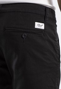 Pantalones cortos de algodón negros con cierre de botón, bolsillo trasero con parche de logo y textura suave en la tela.