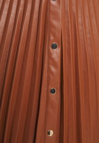 Brun plisserad läskinnkjol med en central knapprem som har runda, glansiga guldfärgade knappar.