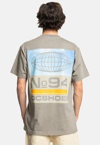 Šedé bavlněné tričko s velkým grafickým motivem na zádech, v modrých a žlutých akcentních barvách, s textem a designem zeměkoule. Krátké rukávy, volnější střih.
