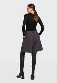 Grijze culotte-shorts met zijzakken en een getailleerde pasvorm, gecombineerd met kniehoge zwarte leren laarzen. Het topje is een aansluitend zwart shirt met lange mouwen.