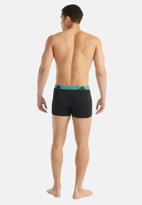 Pánské černé plavky s úzkým střihem, s tyrkysovým elastickým pasem a decentním logem. Hladká látka a krátká délka.