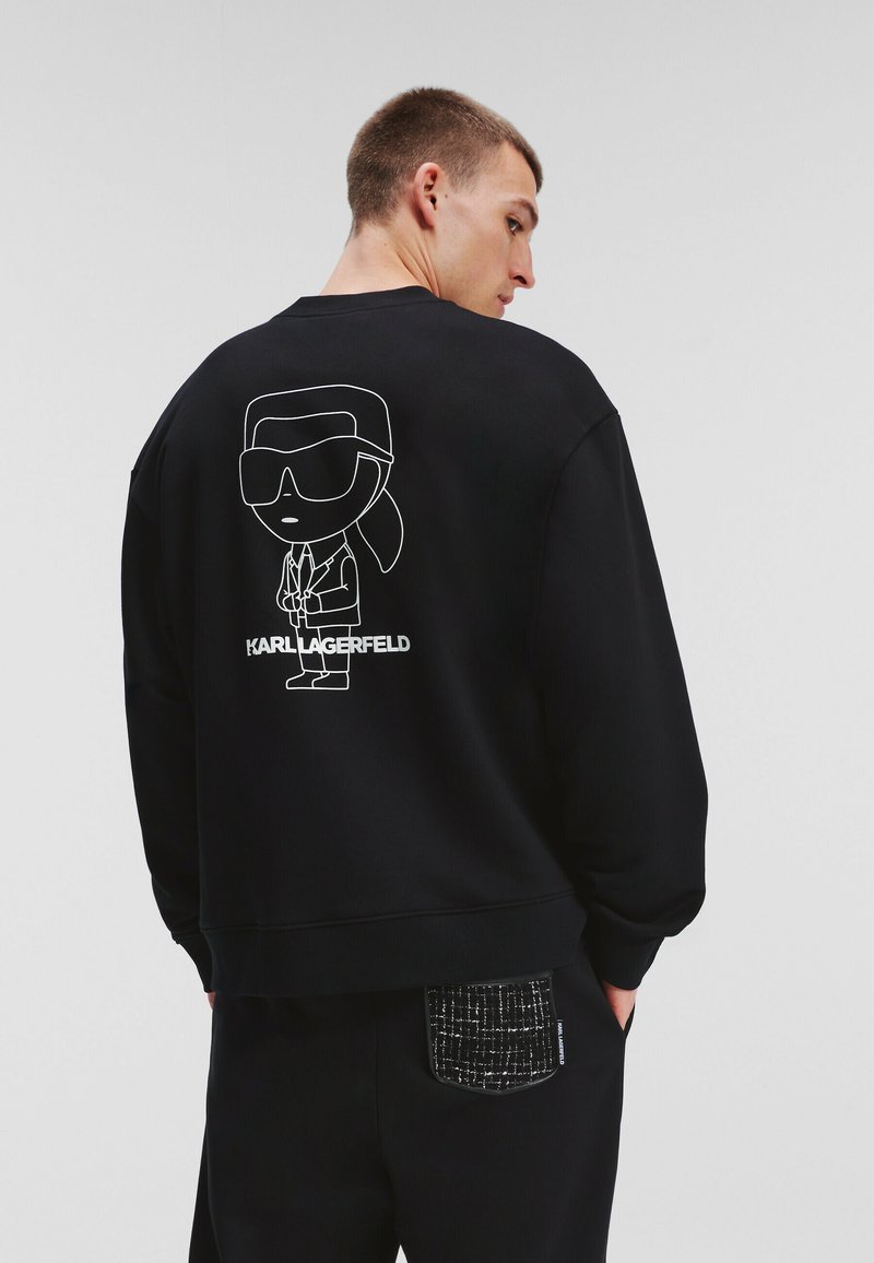 Sudadera negra con una figura de dibujo animado con gafas de sol en la parte trasera y el texto "KARL LAGERFELD" debajo. Tejido suave, corte relajado.