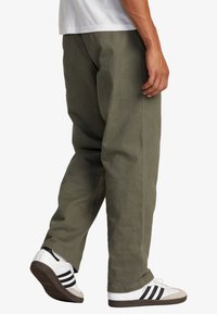 Baggy olijfgroene broek van katoen, met een relaxte pasvorm en zijzakken. Gecombineerd met witte sneakers met zwarte strepen.