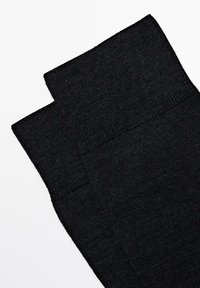 Schwarze gestrickte Socken mit einer glatten Textur, die einen gerippten oberen Rand und eine nahtlose Verarbeitung aufweisen. Flach gefaltet, wobei gleichmäßige Breite und Länge sichtbar sind.