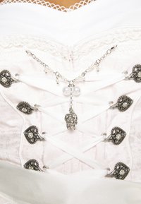 Corset blanc avec des fermoirs argentés à fleurs et un laçage en ruban blanc, orné d'un collier délicat en chaîne argentée et perles.