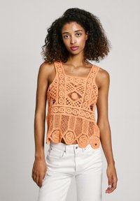 Gehaakte tanktop in oranje met een vierkante halslijn en brede banden. Heeft ingewikkelde patronen en een gegolfde zoom. Gepaard met witte broek.