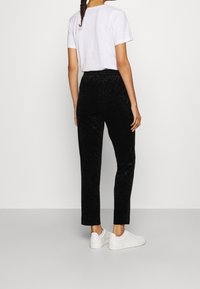Pantalon en velours noir texturé avec une ceinture élastique, coupe droite, associé à un T-shirt blanc uni et des baskets blanches.