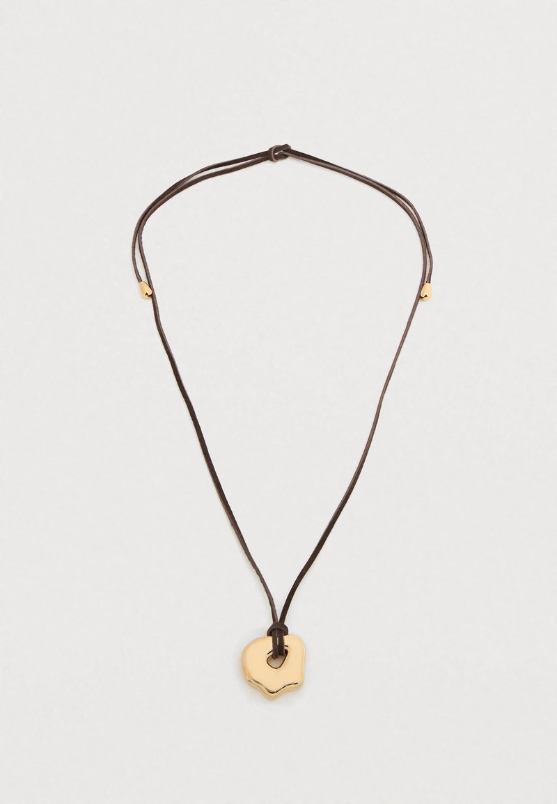 Κολιέ με χρυσό μενταγιόν σε καφέ κορδόνι. Το μενταγιόν έχει στρογγυλεμένο, κυματιστό σχήμα με τμήμα κοπής. Ρυθμιζόμενο μήκος κορδονιού για διαφορετικές εφαρμογές.