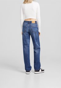 Blaue Jeans aus Denim mit lockerer Passform, sichtbaren Gesäßtaschen und einem Lederpatch am Bund. Kombiniert mit einem weißen gerippten Cropped-Top.