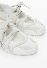 Pantofi sport gri deschis cu un exterior texturat, sistem de șireturi ajustabil și talpă din cauciuc cu mici puncte proeminente pentru aderență.