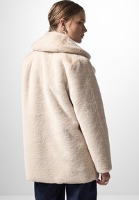 Cappotto in misto lana beige con un ampio colletto, finitura testurizzata e maniche lunghe, mostrato da dietro con una silhouette elegante.