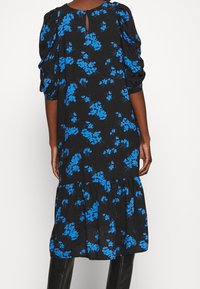 Černé květinové šaty s modrými květy, nabíranými rukávy, klíčovou dírkou na zádech a vrstvami na spodním okraji. Vyrobené z lehkého materiálu s hladkou texturou.