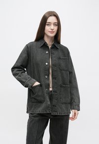 Jeans jakna temno siva, z gumbi spredaj, dvema sprednjima žepoma in ovratnikom. Material ima rahlo teksturiran zaključek.