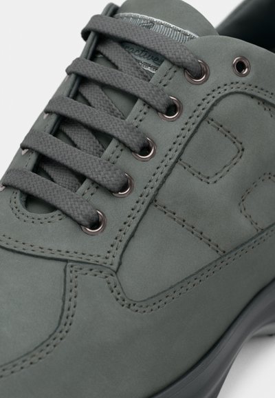 Grå ruskindssko med flade grå snørebånd, metal-øjer og en glat gummisål. Har diskrete syninger og et tekstureret design på siden.