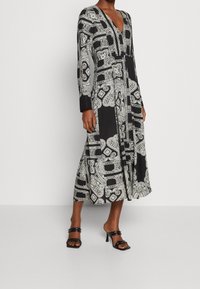 Robe noire et blanche à manches longues avec un décolleté en V, des motifs paisley complexes et une silhouette fluide qui arrive mi-mollet.