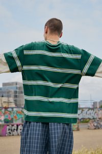 Green striped short-sleeve shirt with horizontal white and yellow stripes, paired with loose plaid trousers. Casual, relaxed fit.