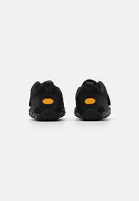 Mustat urheilujalkineet, joissa on kuvioitu pohja, takana vetotappi ja erottuva oranssi Vibram-logo kantapäässä. Pehmeä, joustava materiaali.