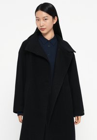 Zwarte wollen mix jas met een brede kraag, relaxed fit en lange mouwen. Beschikt over zijzakken en een subtiele textuur.
