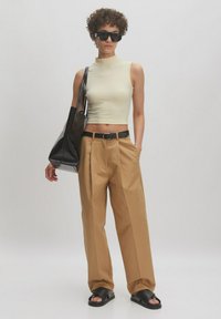 Cream ribbed sleeveless top, tan pleated trousers, black leather belt, oversized black bag, and black slide sandals. Smooth textures throughout.