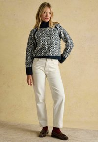 Gestrickter Pullover in marineblau mit weißem Blumenmuster, gerippter Rollkragen, kombiniert mit cremefarbenen Jeans und braunen Mokassins mit kastanienbraunen Socken.