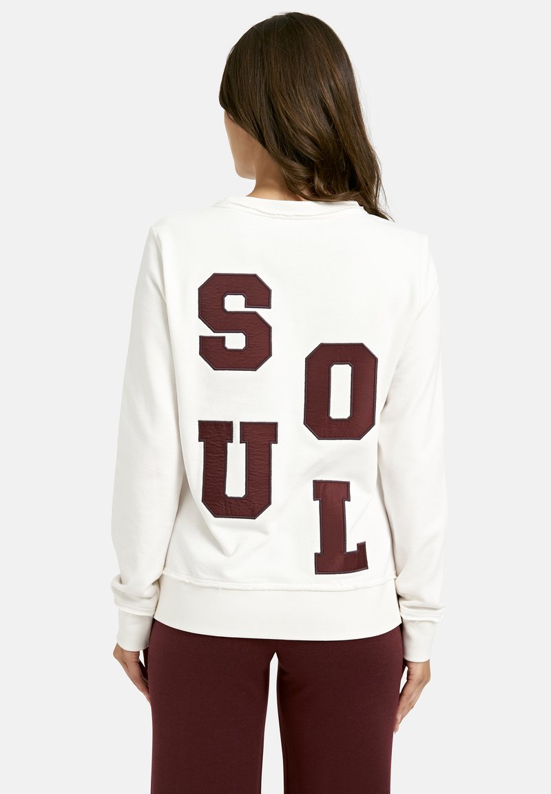 White sweatshirt featuring large burgundy block letters spelling "SOUL" on the back. Ribbed cuffs and hem. Smooth texture.