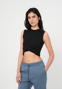 Μαύρο αμάνικο cropped τοπ με σχεδιασμό με στριφογύρισμα μπροστά, συνδυασμένο με ανοιχτό μπλε joggers με ελαστική μέση. Λείο ύφασμα και εφαρμοστή γραμμή.