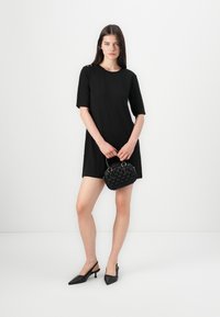 Musta lyhythihainen mekko, jossa on pyöreä pääntie, yhdistettynä teksturoituun mustaan käsilaukkuun ja kolmiomuotoisiin mustiin avokaskenkään.