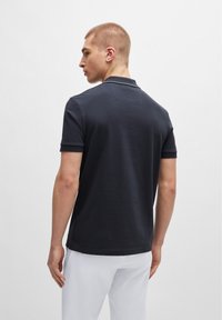 Mørkeblå polo skjorte med klassisk krage, korte ermer og subtile sømdetaljer. Stoffet virker glatt og lett.