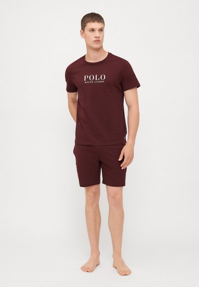 Burgundska bombažna majica s kratkimi rokavi in "POLO" logotipom ter usklajenimi kratkimi hlačami. Ima kratke rokave, okroglo ovratnik in sproščen kroj. Tekstura se zdi gladka.