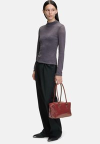 Maglia grigia a maniche lunghe con collo alto, pantaloni neri a gamba larga e una borsa rossa lucida con manici marroni. Texture lisce in tutto.