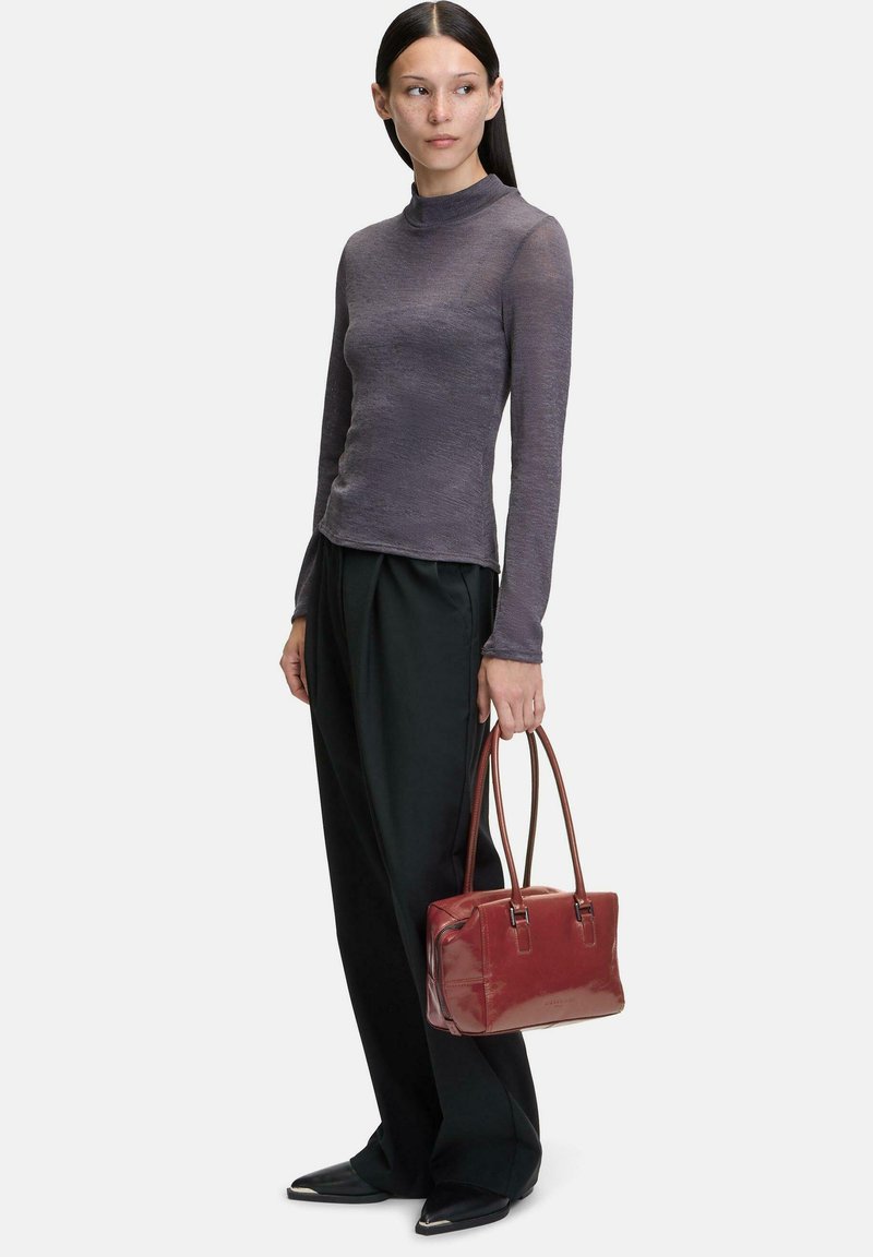Maglia grigia a maniche lunghe con collo alto, pantaloni neri a gamba larga e una borsa rossa lucida con manici marroni. Texture lisce in tutto.