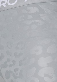 Pantalones cortos deportivos de color gris claro con un sutil patrón de leopardo. Cuenta con una cinturilla elástica blanca con marca. Textura suave.
