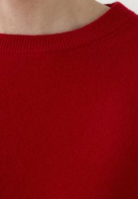 Punainen neulepaita, jossa on pyöreä pääntie ja ribbineulos. Tekstuuri näyttää pehmeältä ja sileältä, ja siinä on yhtenäinen väri ilman näkyviä kuvioita.