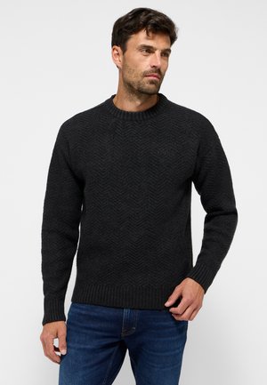 Dunkelgrauer Strickpullover mit einem strukturierten Fischgrätmuster, Rundhalsausschnitt und gerippten Bündchen. Über einer blauen Jeans getragen.