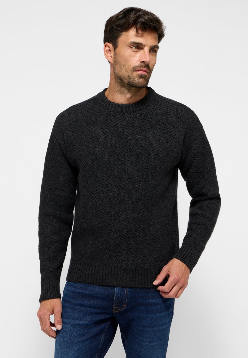Dunkelgrauer Strickpullover mit einem strukturierten Fischgrätmuster, Rundhalsausschnitt und gerippten Bündchen. Über einer blauen Jeans getragen.