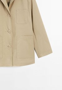 Beige, letvægtsjakke med krave-design, tre forreste knapper og to store påsyede lommer på fronten. Glat tekstur.