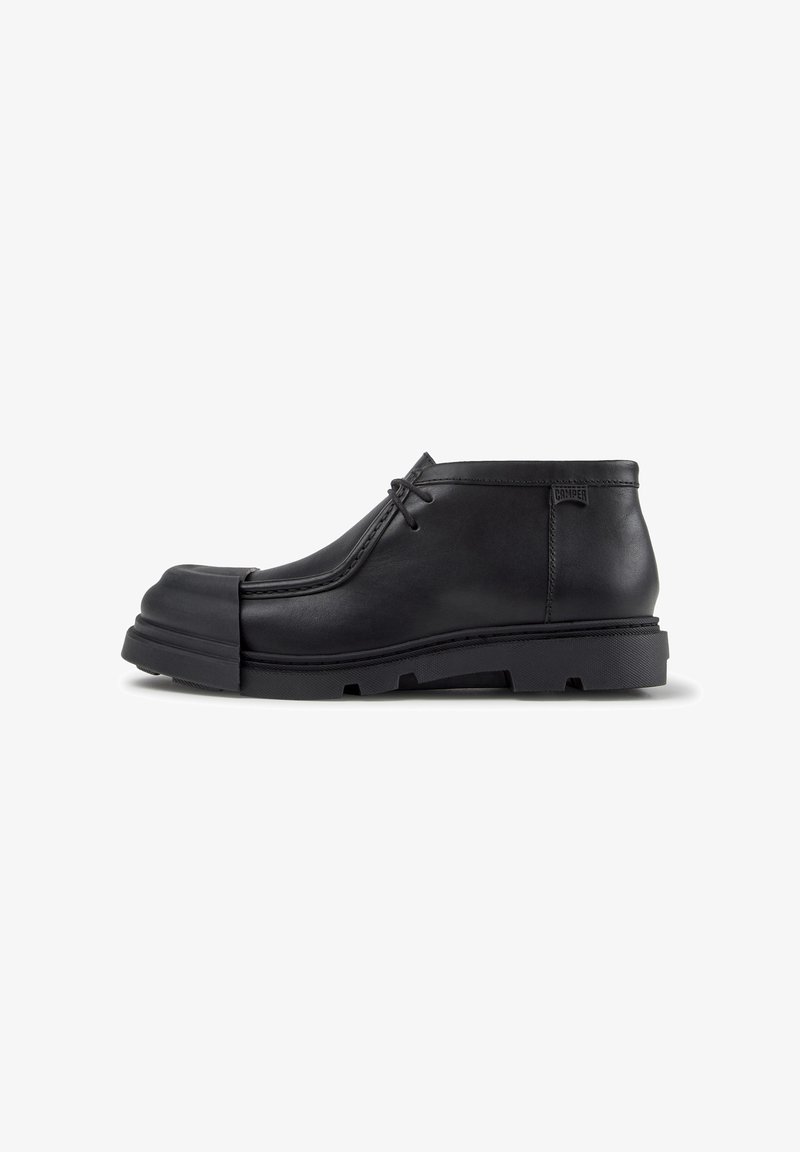 Chaussure en cuir noir à lacets avec un embout arrondi et une semelle en caoutchouc épaisse, vue latérale sur fond blanc.